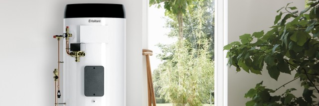 a Vaillant hot water cylinder near a door with a pair of wellies and a shovel. There is a green plant in a white pot to the right a Vaillant hot water cylinder near a door with a pair of wellies and a shovel. There is a green plant in a white pot to the right