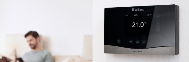 a man sat on a sofa on his phone with a Vaillant senso heating control on a white wall a man sat on a sofa on his phone with a Vaillant senso heating control on a white wall